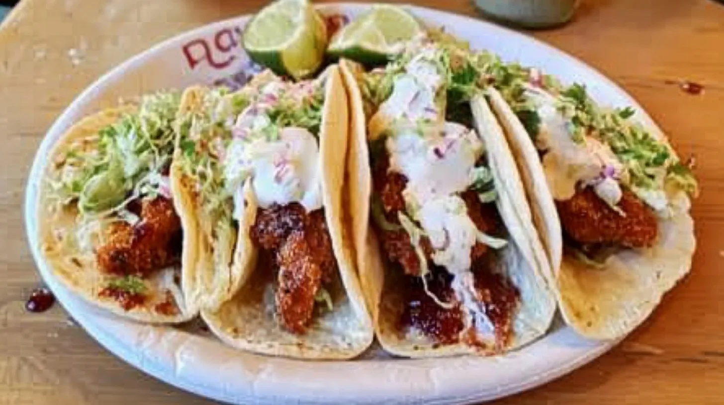 Fresh fish tacos served in corn tortillas, topped with cabbage slaw, avocado, and a creamy sauce.
